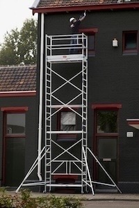 Façadier enduisant le haut d’un bâtiment avec un échafaudage roulant. Il lui permet de travailler toute la longueur du bâtiment sans devoir défaire à chaque fois l’échafaudage. Le garde-corps lui évite les déséquilibres et les chutes malgré ses mouvements brusques