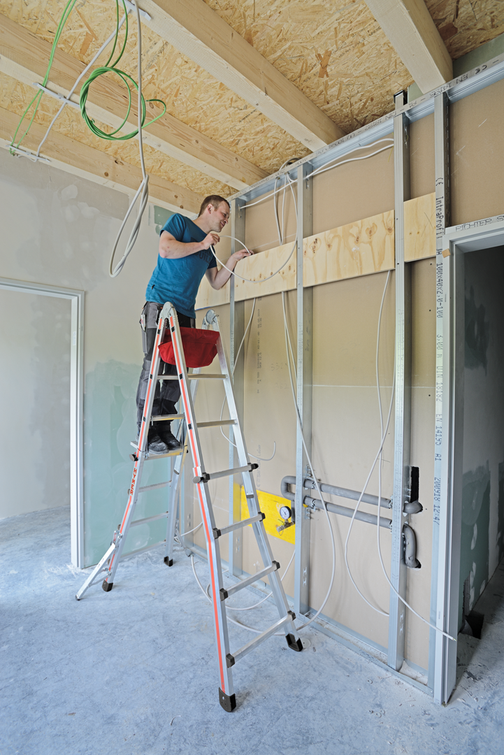 Electricien en équilibre stable sur une échelle télescopique installant le système électrique